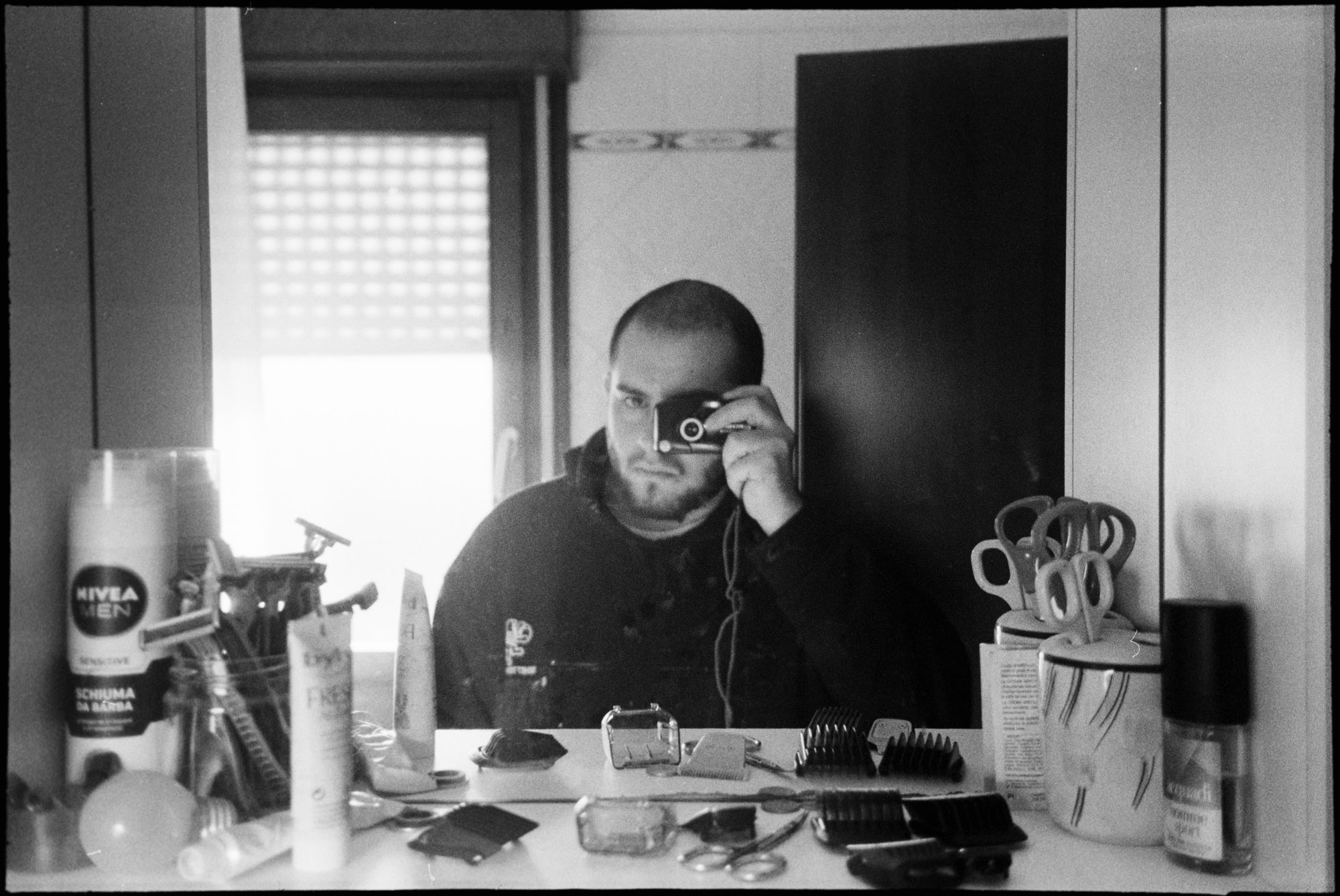 Black and white self-portrait with a camera at a table